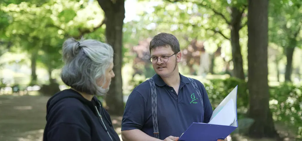 Johannes Siegele im Gespräch mit einer älteren Frau unter Bäumen