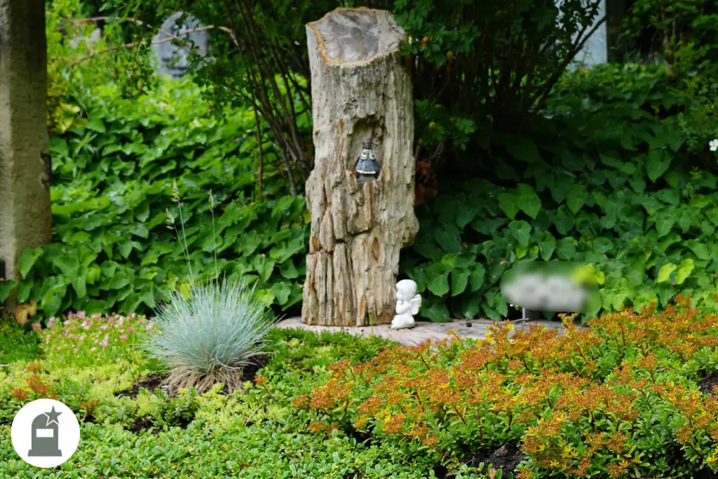 Grabmal aus Holzstamm in orange blühender Bepflanzung