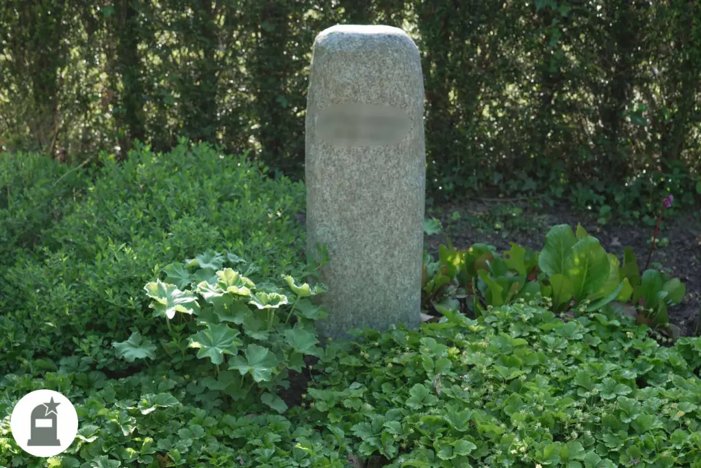 Hohe Granitstele in dichter grüner Bepflanzung