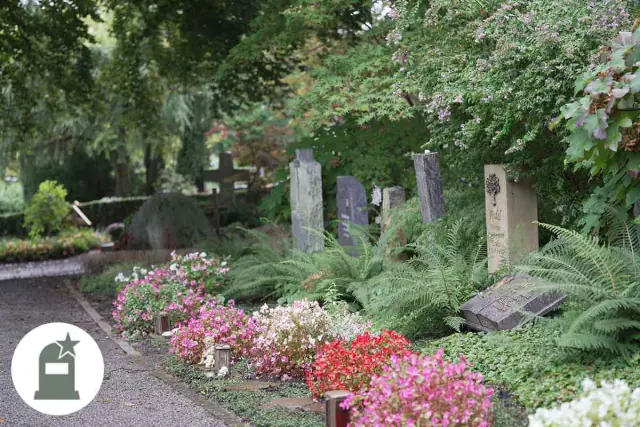 Grabfeld mit Stelen, Farnen und rosa und roten Begonien am Weg