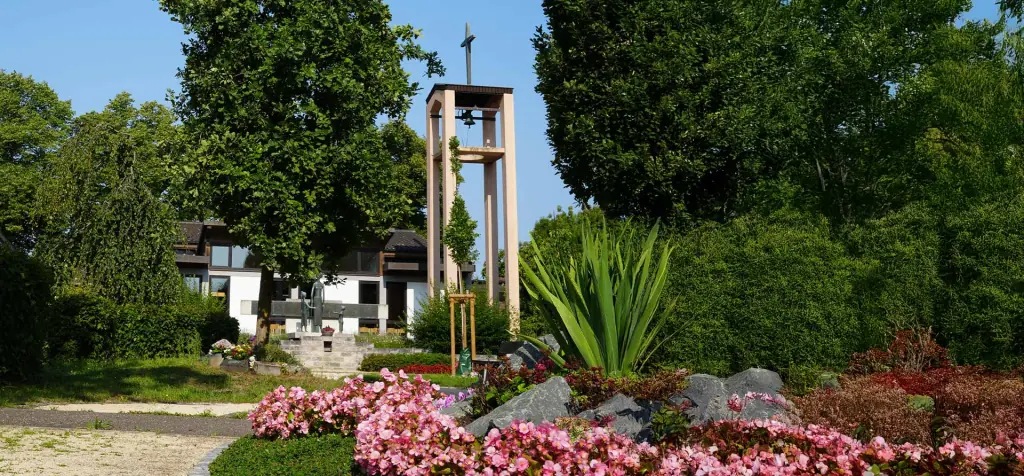 Glockenturm und blühendes Grabfeld am Friedhof Spöck