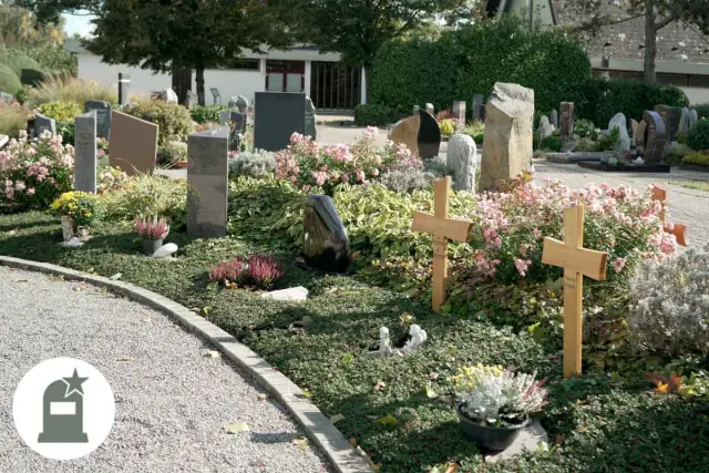 Grabfeld mit Holzkreuzen und rosa Blüten am Weg