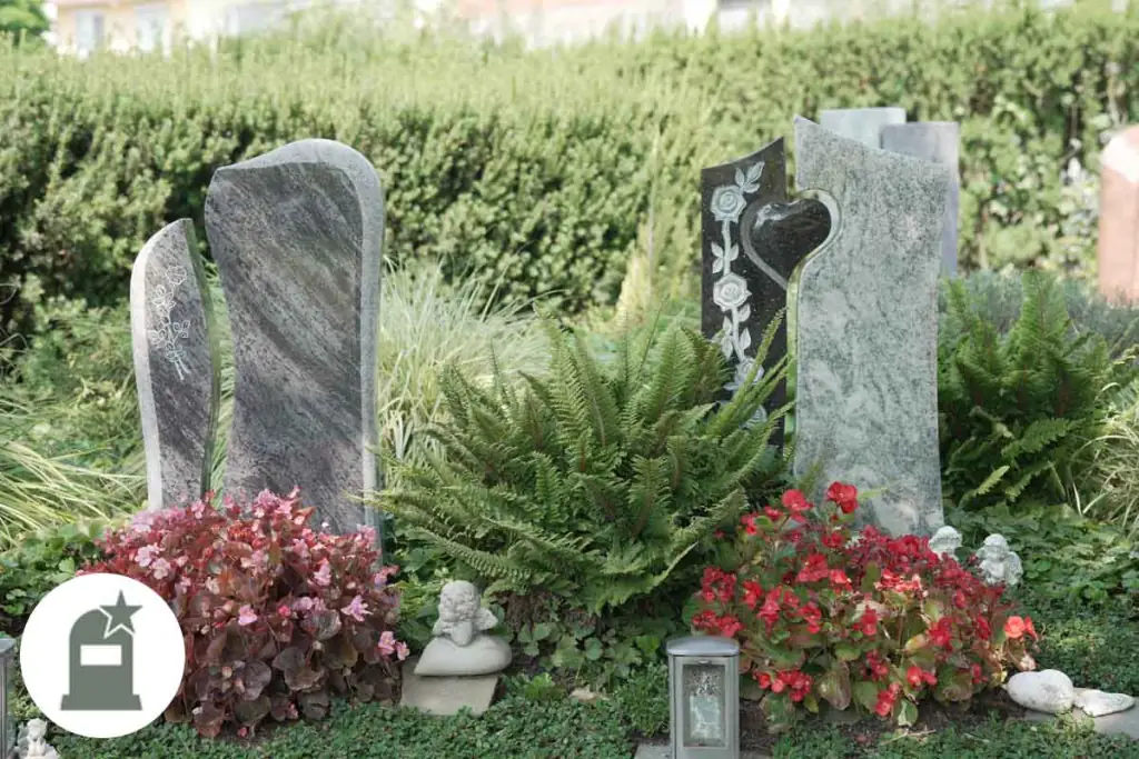 Zwei Grabstelen mit Herz-Motiv zwischen Farnen und roten Blumen