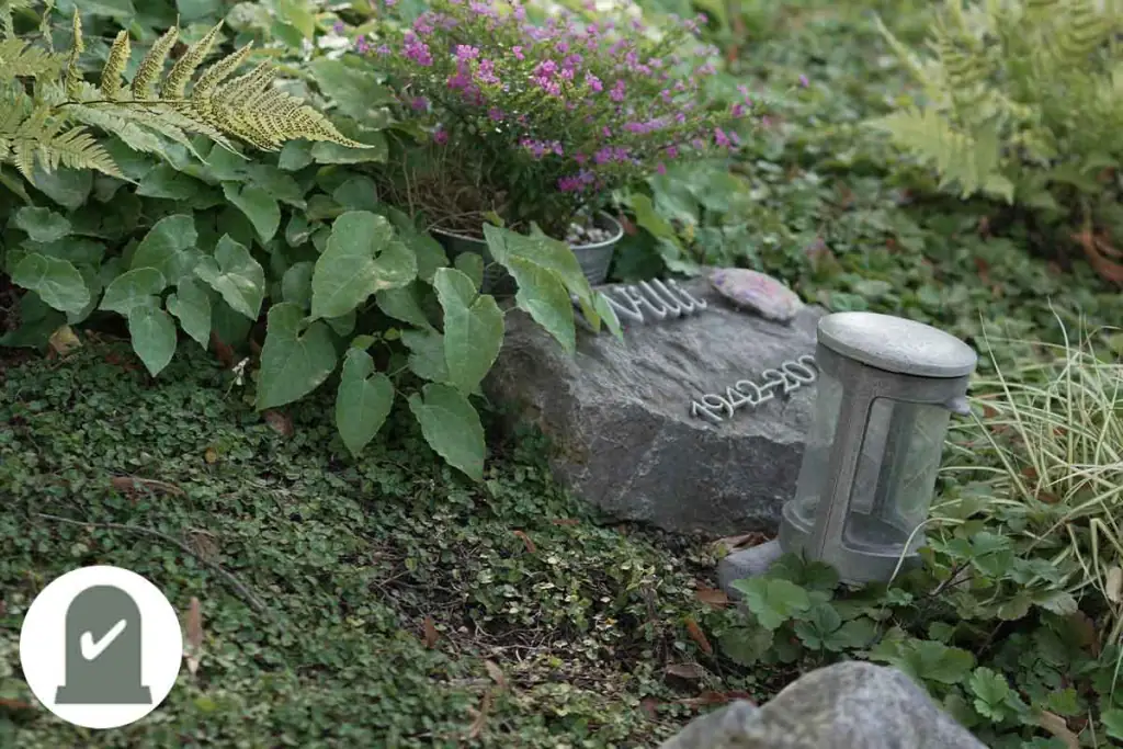 Liegender Grabstein mit Laterne zwischen Farnen