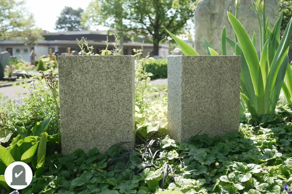 Zwei helle Granitstelen hinter grüner Bepflanzung